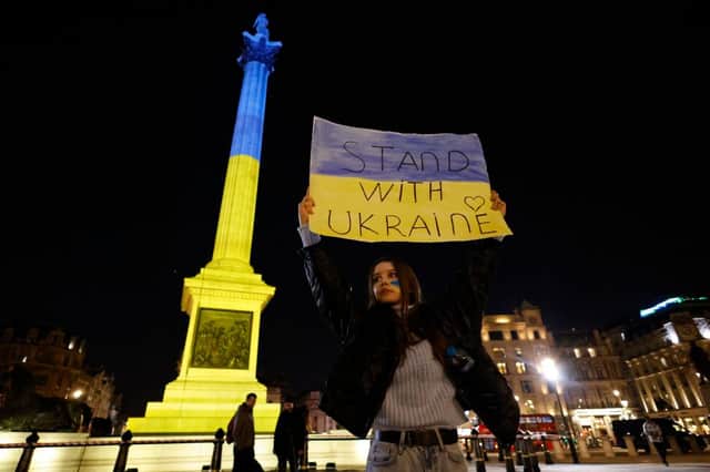 A protester stands with a placard as the colours of the Ukrainian flag are projected onto Nelson’s Column in Trafalgar Square. Credit: TOLGA AKMEN/AFP via Getty Images