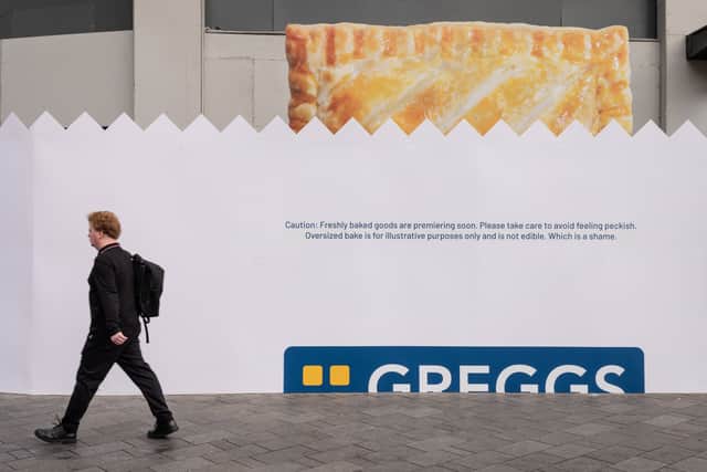 Passers-by walk past the hoardings for the new Greggs store to be opened in Leicester Square, London. Credit: SWNS