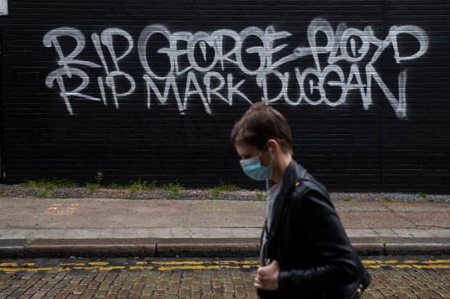 A woman wearing a face mask walks past a wall with graffiti that reads, RIP George Floyd RIP Mark Duggan’ in Shoreditch. Photo: Getty