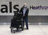A man wearing a mask stands at the international arrivals gate at Heathrow Terminal 5.