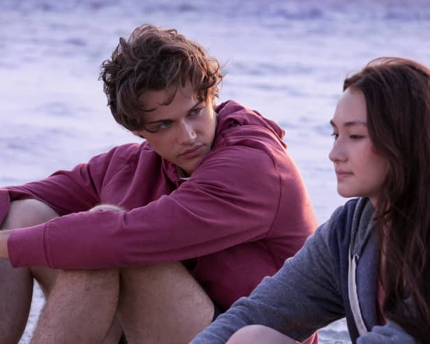 Christopher Briney as Conrad and Lola Tung as Belly, sat together by the ocean at sunset (Credit: Dana Hawley/Prime Video)