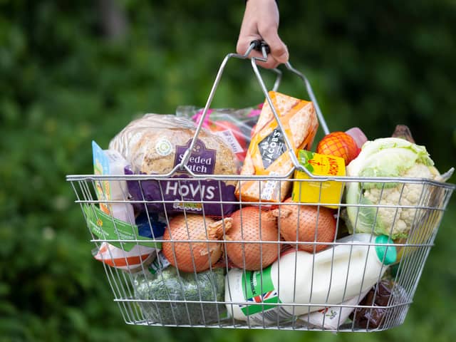 A woman holds a shopping basket of groceries.