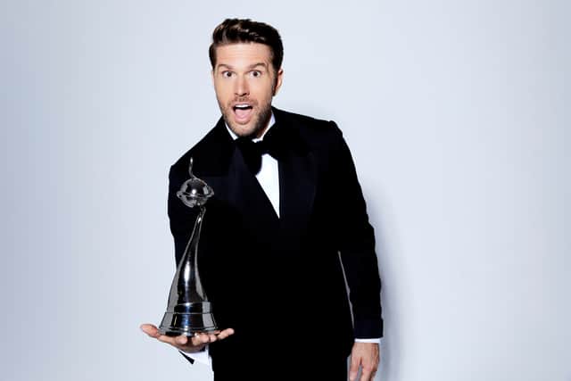 Joel Dommett, wearing a tuxedo, balancing an NTA trophy in the palm of his right hand (Credit: ITV)
