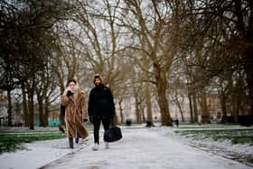 A couple walks in a park in the snow in central London.