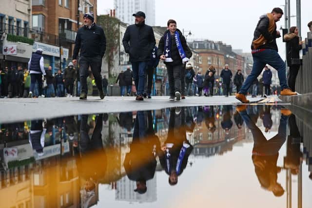 Football fans are reflected in a puddle of rainwater as they arrive for the English Premier League football match between Tottenham Hotspur and Crystal Palace at Tottenham Hotspur Stadium