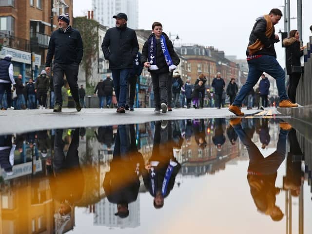 Football fans are reflected in a puddle of rainwater as they arrive for the English Premier League football match between Tottenham Hotspur and Crystal Palace at Tottenham Hotspur Stadium 
