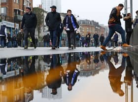 Football fans are reflected in a puddle of rainwater as they arrive for the English Premier League football match between Tottenham Hotspur and Crystal Palace at Tottenham Hotspur Stadium 