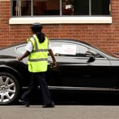 A parking enforcement officer posts notices on the car after a wheel clamp has been attached in Kensington