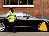 A parking enforcement officer posts notices on the car after a wheel clamp has been attached in Kensington