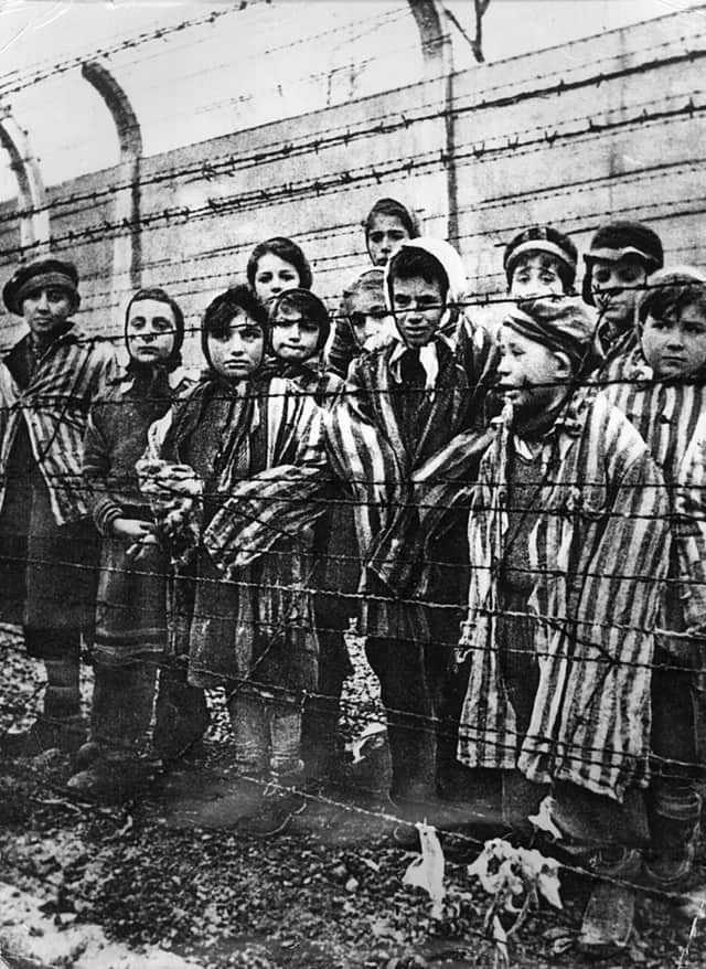 A group of child survivors behind a barbed wire fence at the Nazi concentration camp at Auschwitz-Birkenau on liberation day.