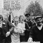 The wedding of Peter Oxley and Alena Czeknovska at Caxton Hall clashes peaceably with a dustmen's protest during a period of industrial action, 3rd October 1969. Dustman Billy MaGinnis waves a placard behind the heads of the happy couple.  (Photo by Norman Potter/Express/Getty Images)