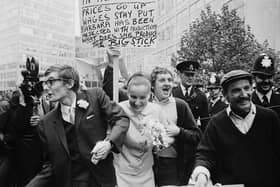 The wedding of Peter Oxley and Alena Czeknovska at Caxton Hall clashes peaceably with a dustmen's protest during a period of industrial action, 3rd October 1969. Dustman Billy MaGinnis waves a placard behind the heads of the happy couple.  (Photo by Norman Potter/Express/Getty Images)
