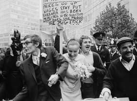 The wedding of Peter Oxley and Alena Czeknovska at Caxton Hall clashes peaceably with a dustmen's protest during a period of industrial action, 3rd October 1969. Dustman Billy MaGinnis waves a placard behind the heads of the happy couple.  (Photo by Norman Potter/Express/Getty Images)