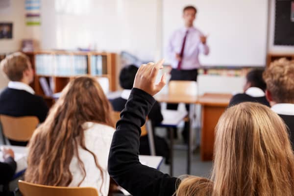 A female student raising her hand to ask a question in class. Credit: Monkey Business.