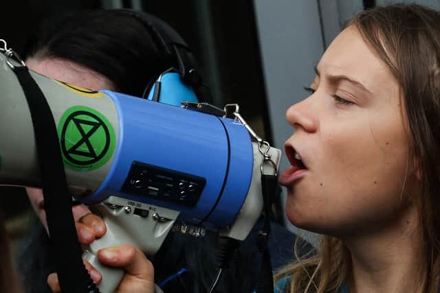 Swedish climate activist Greta Thunberg chants slogans in loud speaker as she sits in front of the entrance of the Bank JPMorgan in Canary Wharf. Credit: Daniel Leal/AFP via Getty Images.