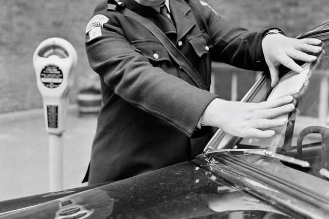 A traffic warden fixing a ticket to the windscreen of an illegally parked car in London on September 19th, 1960.