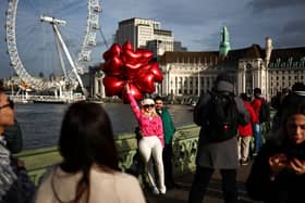 A couple poses with ballons shaped as hearts on Westminster bridge with the London Eye on the background