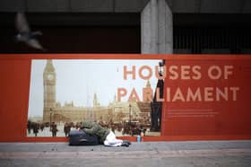 A rough sleeper lies on a suitcase in front of an advertisement board showing the Houses of Parliament in central London