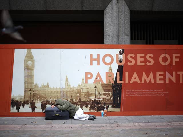 A rough sleeper lies on a suitcase in front of an advertisement board showing the Houses of Parliament in central London