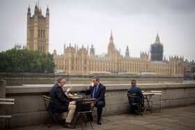 People have coffee on the Thames Embankment with the Houses of Parliament in the background