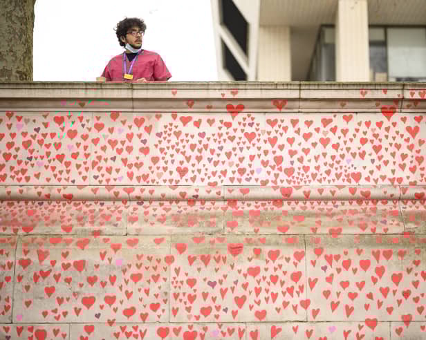 A man wearing medical clothing looks out from above the Covid-19 Memorial Wall outside St Thomas' Hospital in London