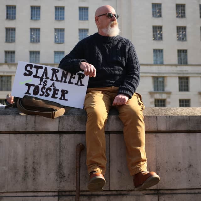 A man sits on a wall with a sign saying 'Starmer is a tosser' as people take part in a farmer's protest over the changes to inheritance tax rules on farms