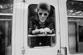 Pop musician David Bowie leaning out of a train window at London Victoria railway station. 