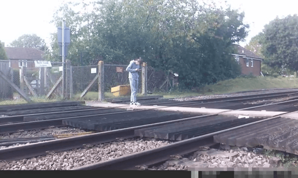 Teen stares at phone while stood on level crossing. Network Rail 