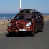 A zombie themed vehicle driving on a road by the coast