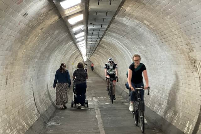 Two cyclists speeding through the Greenwich Foot Tunnel while a pushchair passes by