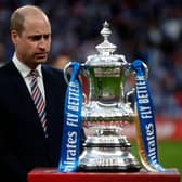 Britain's Prince William, Duke of Cambridge stands by the winner's trophy as the Leicester players celebrate victory after the English FA Cup final football match between Chelsea and Leicester City at Wembley Stadium in north west London on May 15, 2021.