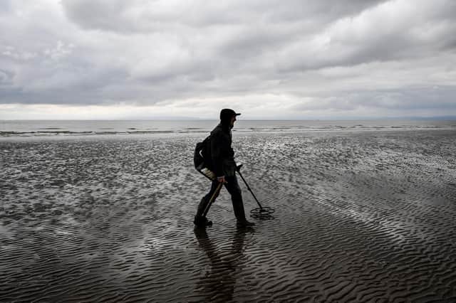 A man uses a metal detector on Barry Island beach, Wales.