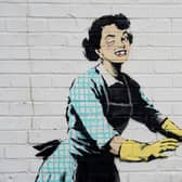 Undated handout file photo of one of the new works by Banksy, appears to show a 1950's housewife, wearing a classic blue pinny and yellow washing up gloves, with a swollen eye and a missing tooth seemingly shoving her male partner into a chest freezer, the piece is set on a white wall backdrop in Kent. Issue date: Tuesday February 14, 2023.