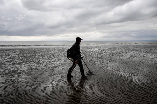 A man uses a metal detector on Barry Island beach, Wales.