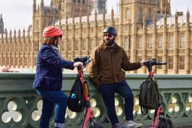 A man and woman with Voi scooters on Westminster Bridge, with the Houses of Parliament behind them.