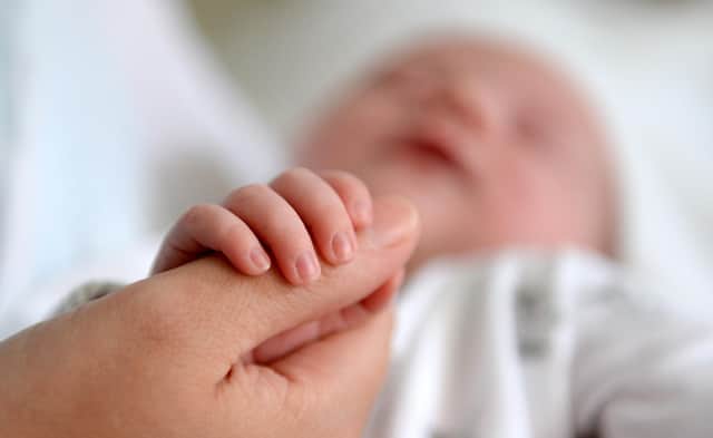 A new born baby grasps the thumb of her mother