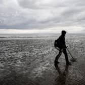A man uses a metal detector on Barry Island beach, Wales.